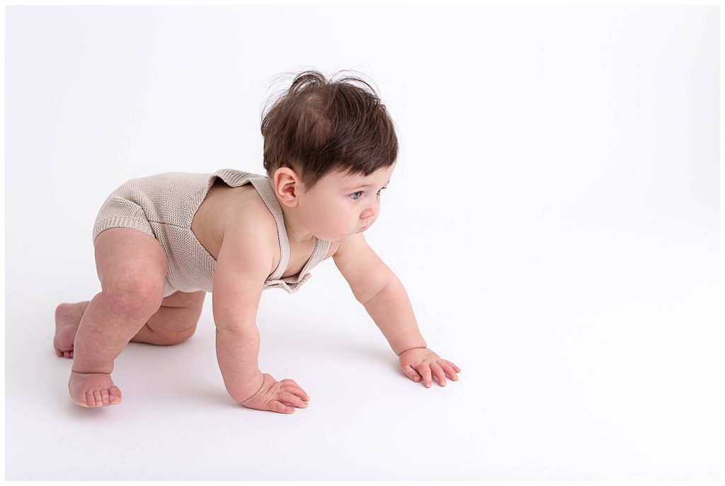 Nine month old breastfed baby crawling to the right of the image on a white backdrop. This blog post is about breastfeeding must-haves. 