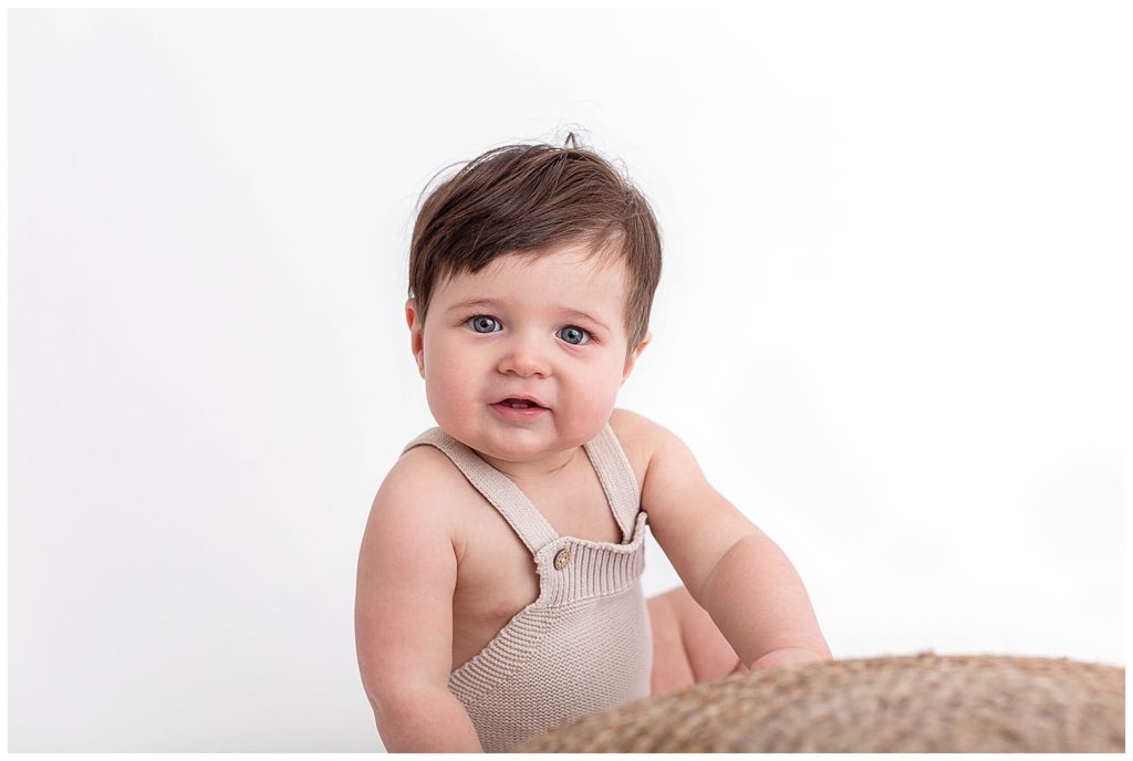 Nine Month old baby in beige romper looking at camera.