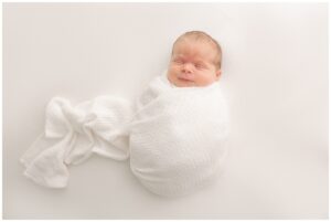Newborn Baby wrapped in white swaddle on white backdrop. In a blog post about baby boutiques in Portland Oregon. 