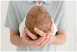 Close up image of baby head being held in dad's hands. Dad is wearing a baby blue polo shirt. 