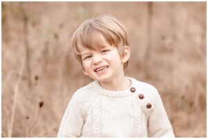 toddler boy in cream sweater smiling at the camera in a field of tall golden grass. Family Photography Session in Portland, Oregon. 