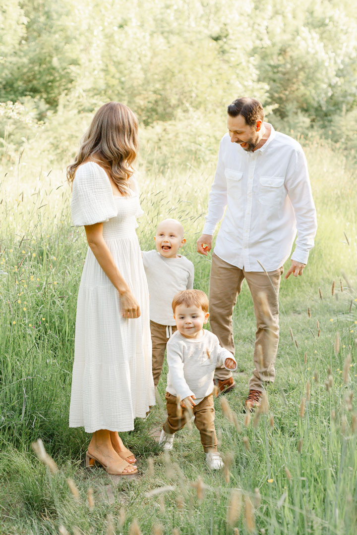 Family of four out in a tall grassy field laughing together and playing. Family Photo session tips