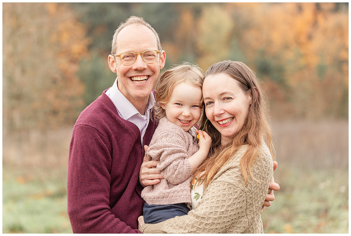 Family of three, dad, three year old girl and mom are all snuggled together at their fall family photo session in Portland, Oregon.
