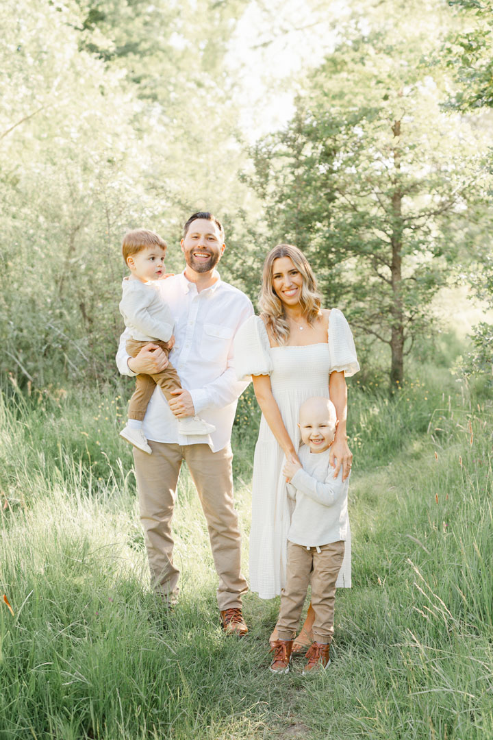 Family Photography Session Tips. Family of 4 standing out in nature and smiling at the camera. Family is wearing light, neutral tones and colors