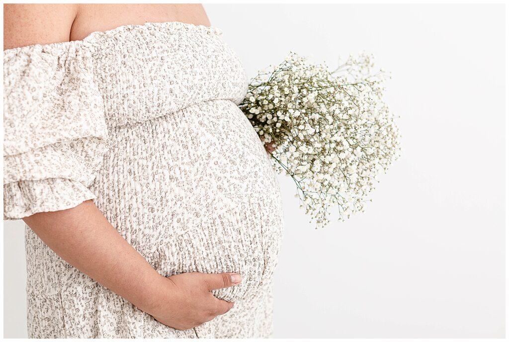 Close-up image of pregnant belly and mom holding a bouquet of baby's breath.