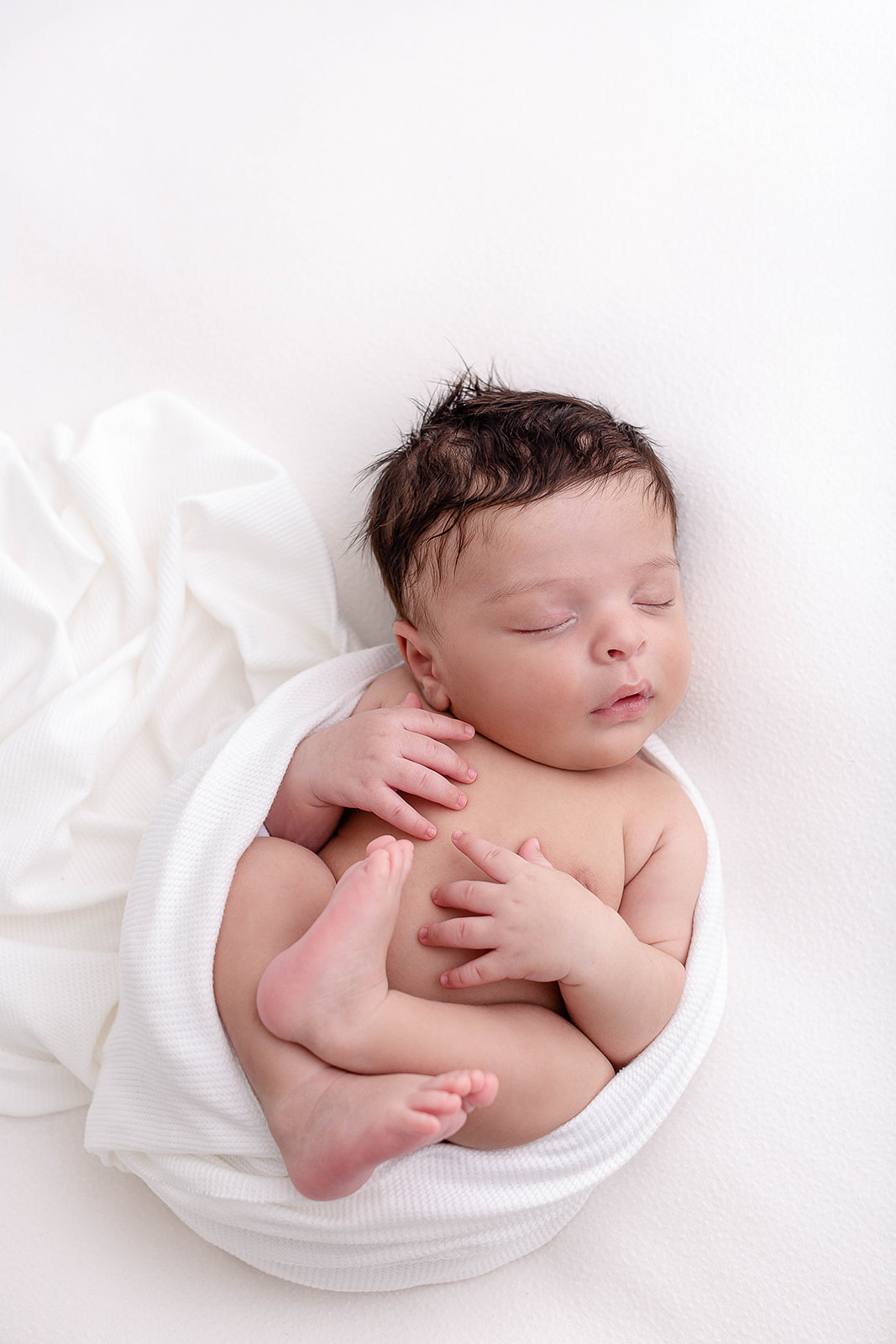A newborn baby sleeps in a white swaddle