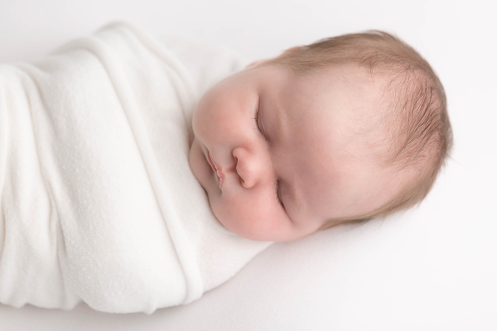 A newborn baby sleeps wrapped up tight in a white swaddle Portland Midwifery