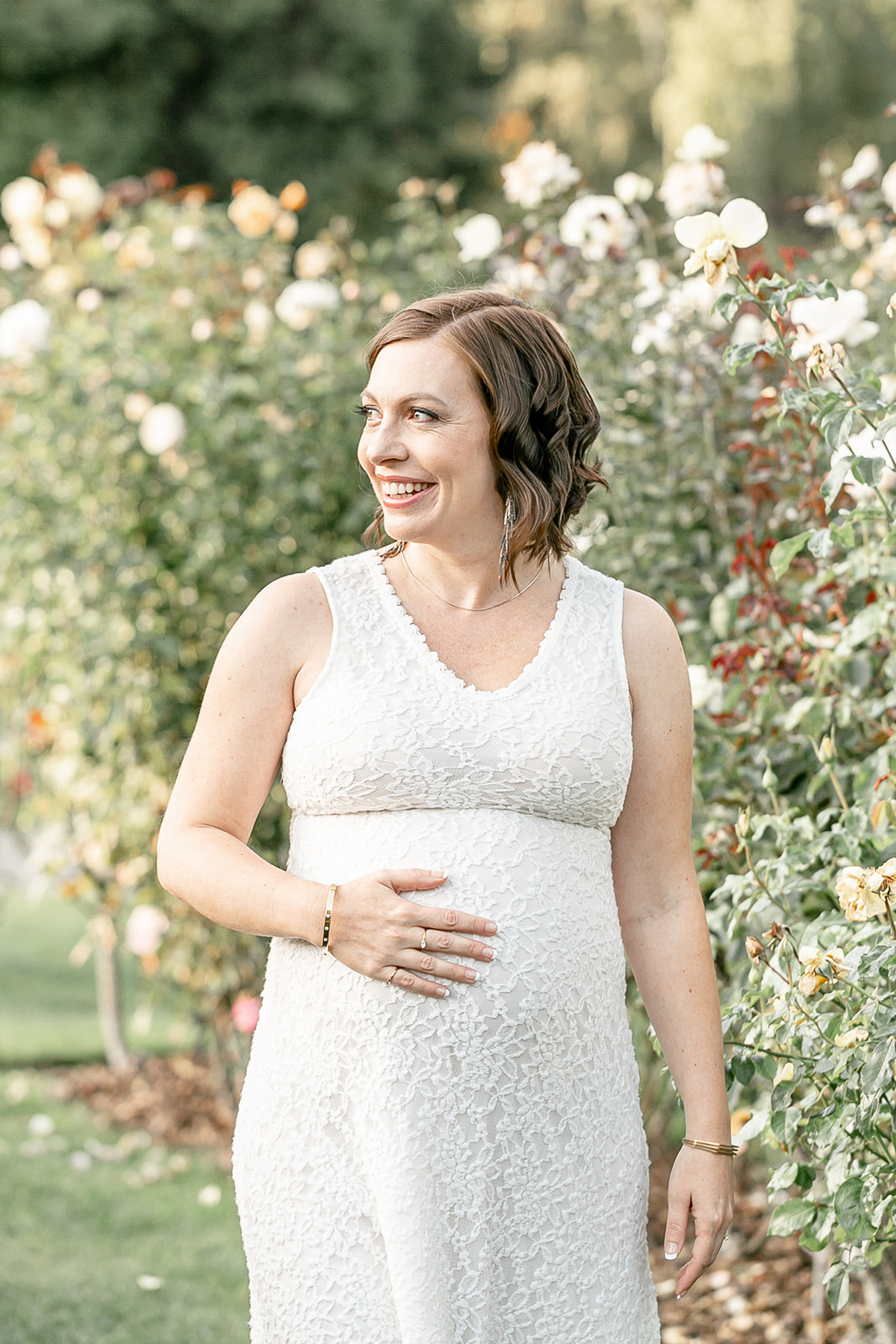 A mother to be in a white lace dress walks through a garden of white roses Portland Date Night Ideas