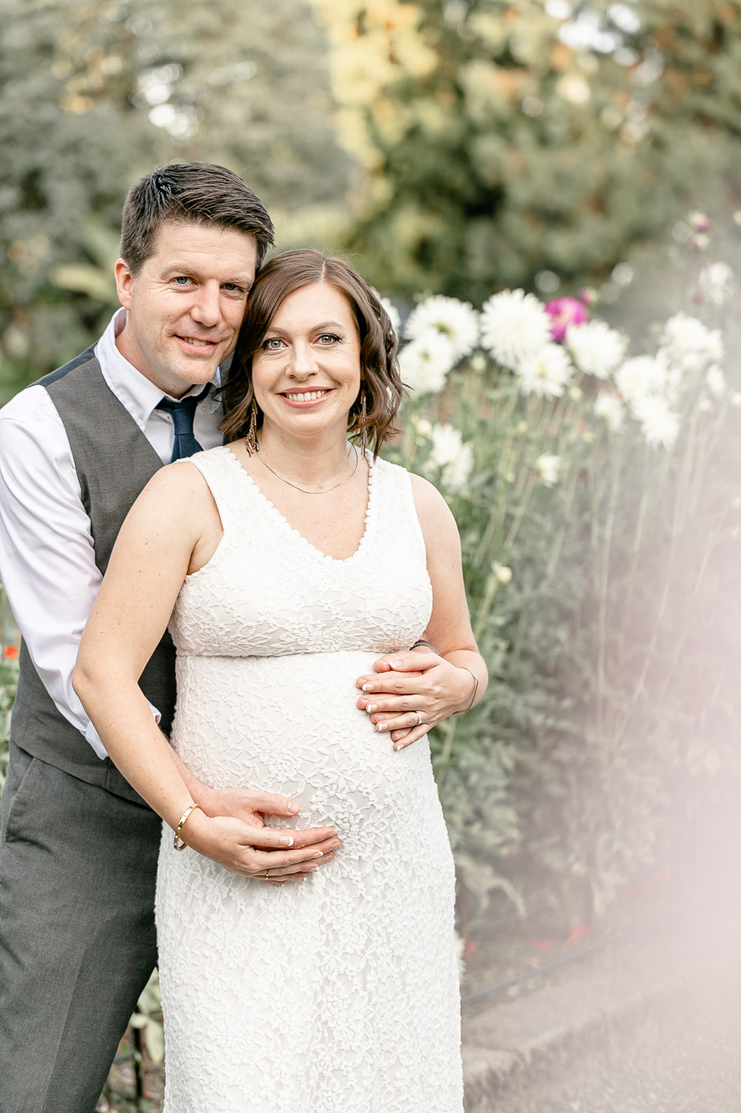 A mother to be and her husband stand together in a flower garden path Portland Date Night Ideas