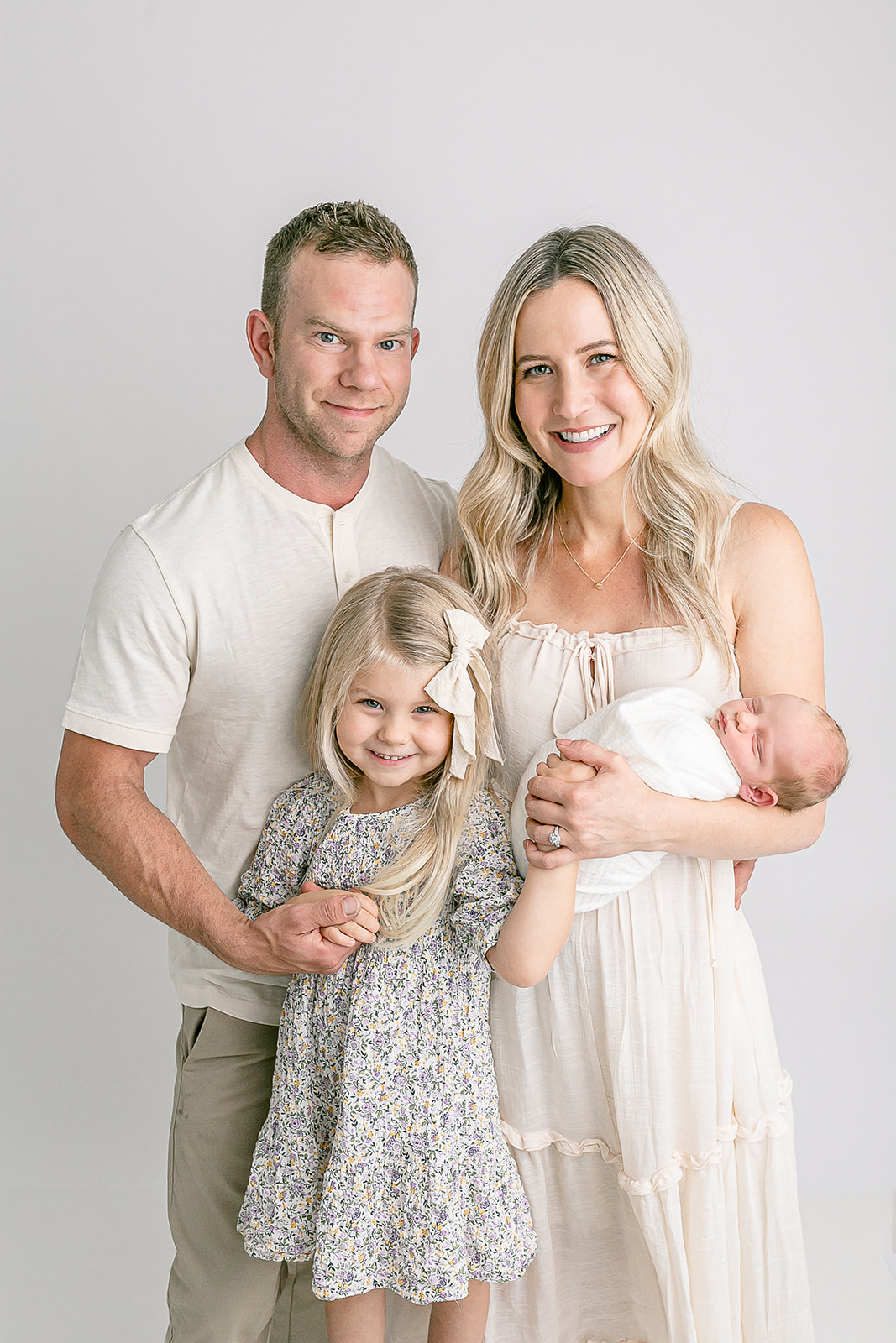 A family of four stand together in a studio while mom holds the newborn baby Portland Doulas