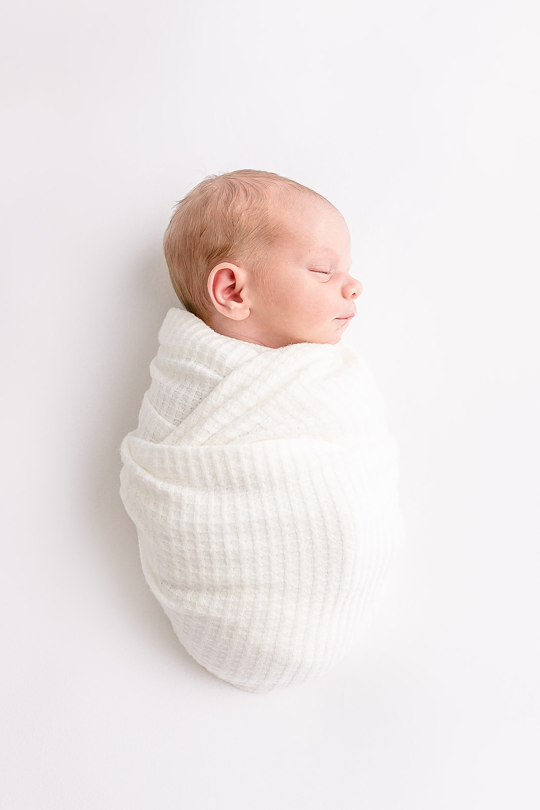 A newborn baby sleeps in a white swaddle in a studio Portland Doulas