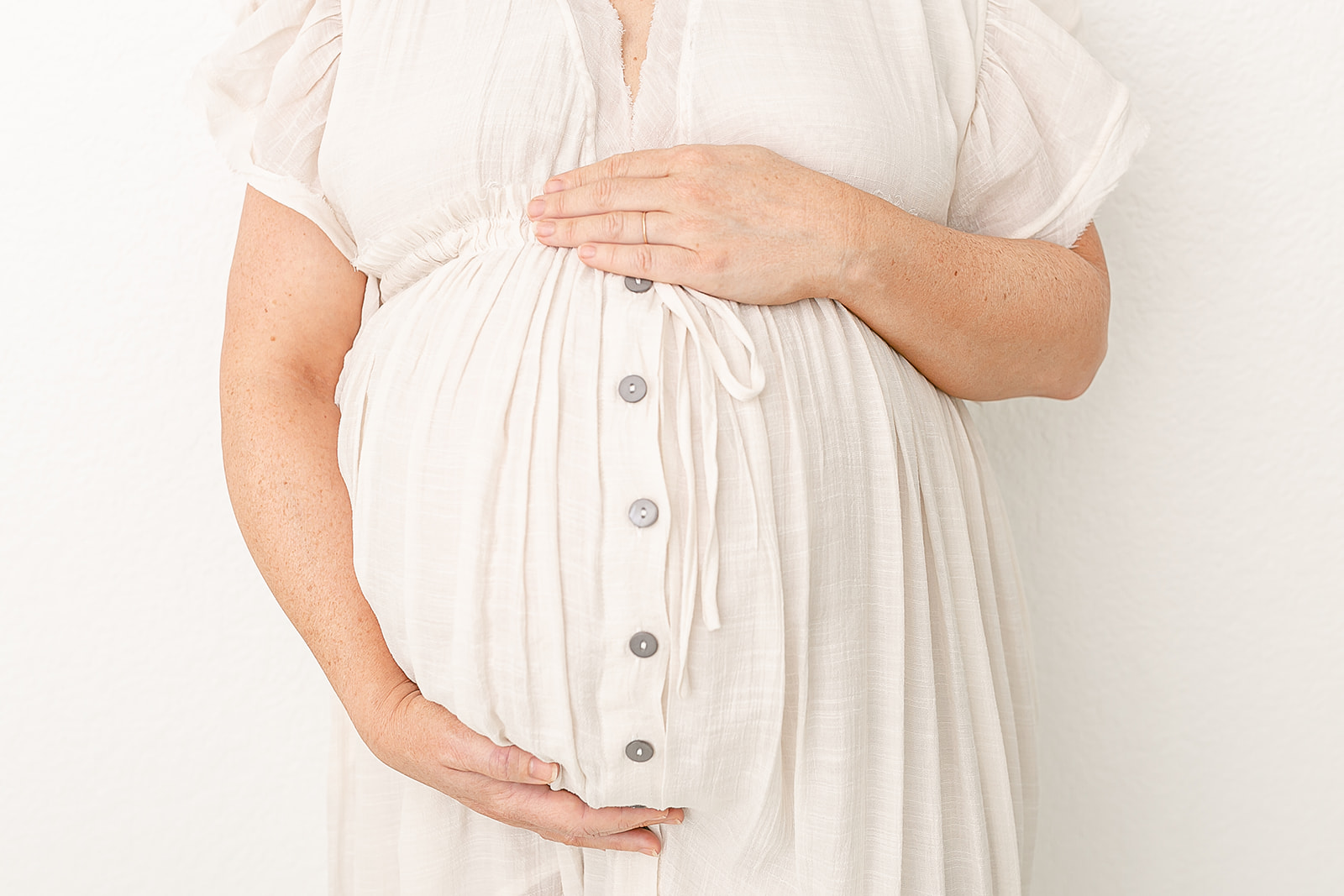 Details of a mother to be standing in a studio with hands on her bump in a white dress Portland prenatal massage