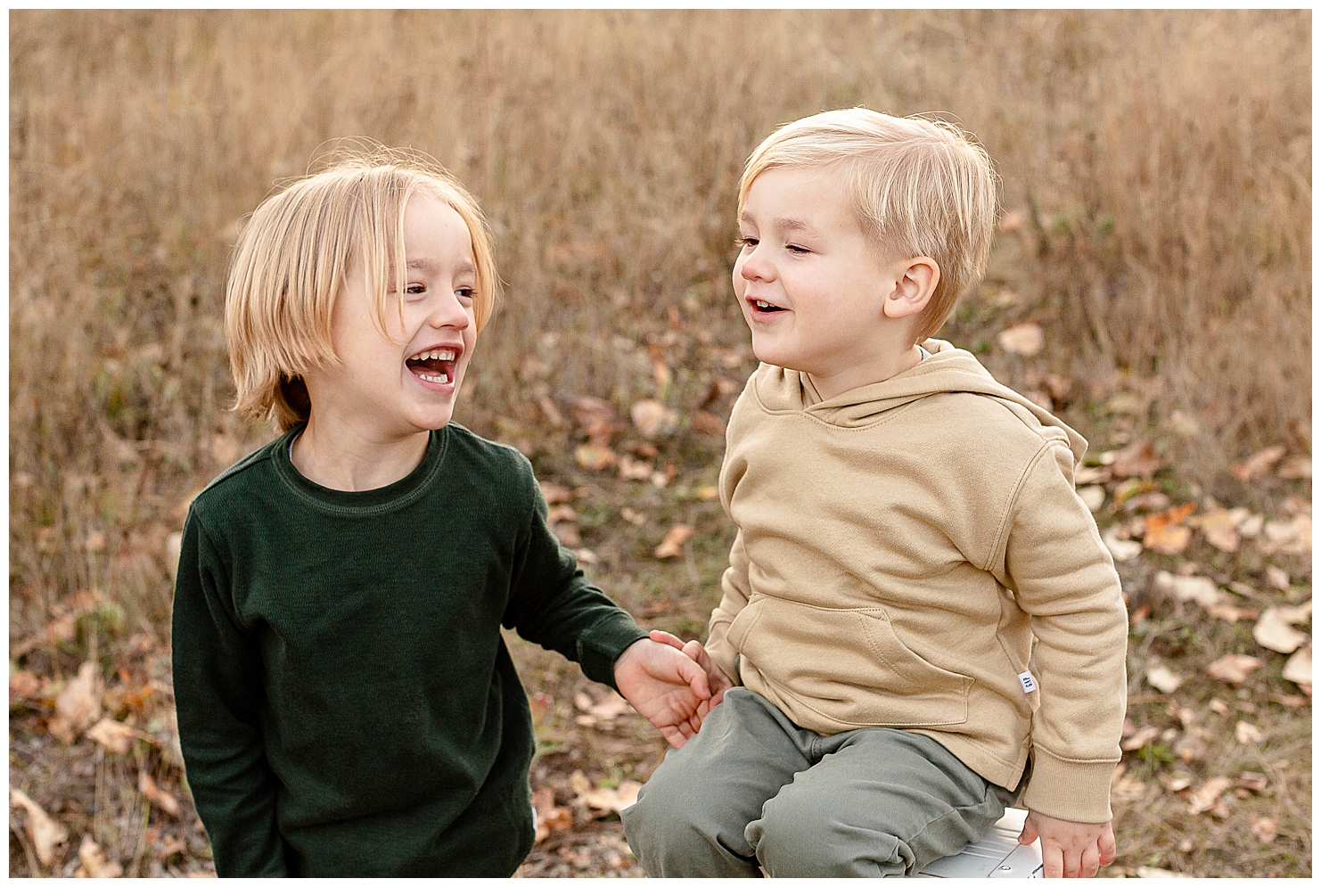 Two young brothers are laughing towards each other at their fall family portraits.