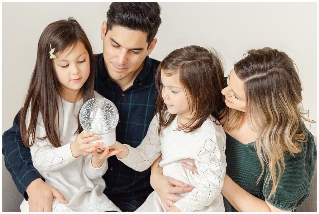 family of four all sitting down together and looking at a snow globe with a white christmas tree in it.