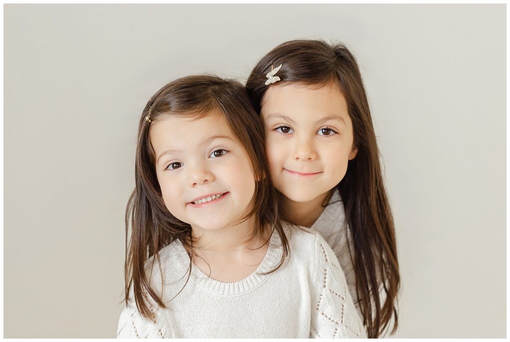 Two young sisters with heads together and smiling at the camera. Ashlie Behm Photography