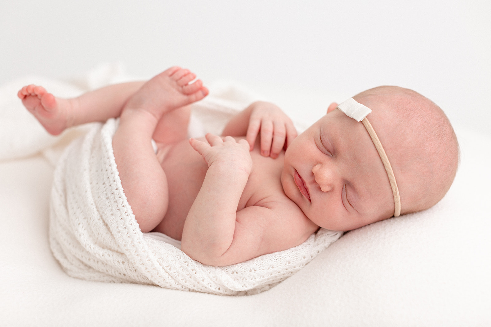 A newborn baby sleeps on a cushion in a white blanket before visiting a Portland pediatrician