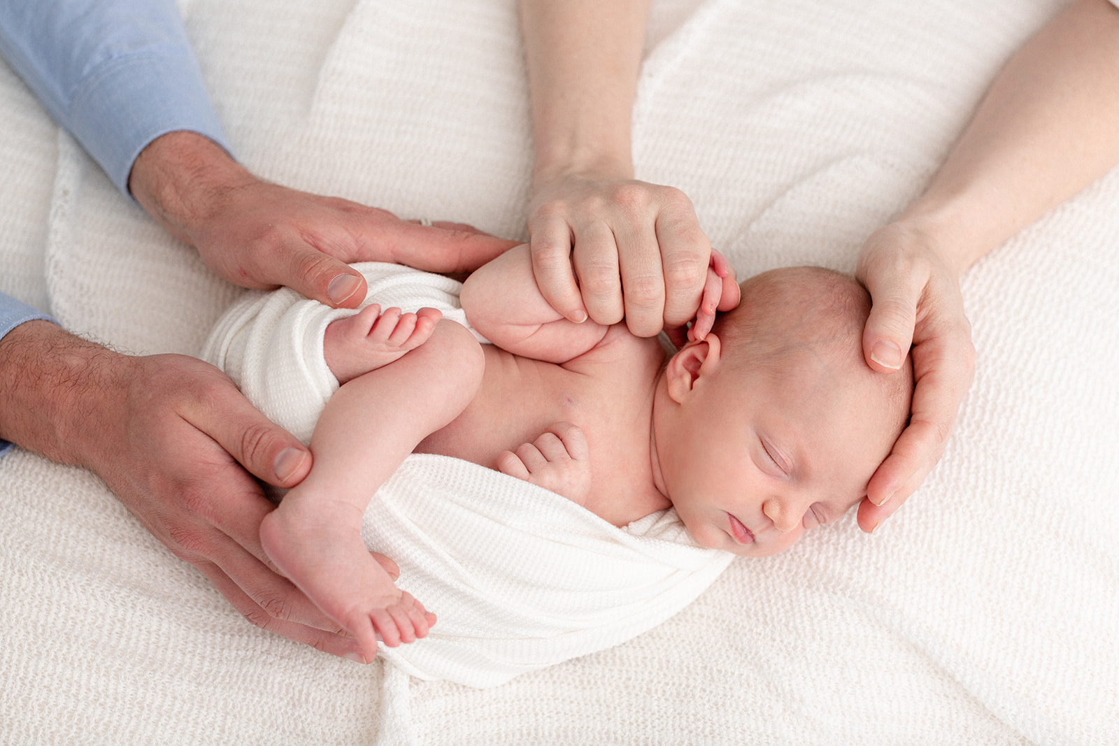 A newborn baby sleeps while being held by mom and dad's hands