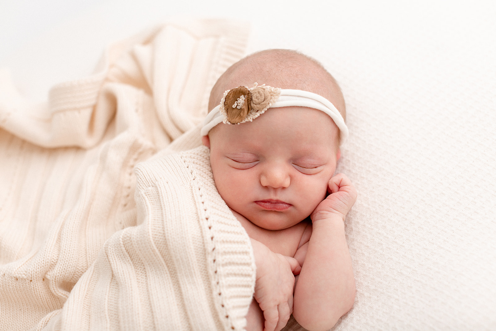 A newborn sleeps on a white bed under a knit blanket after visiting Posh Baby Portland