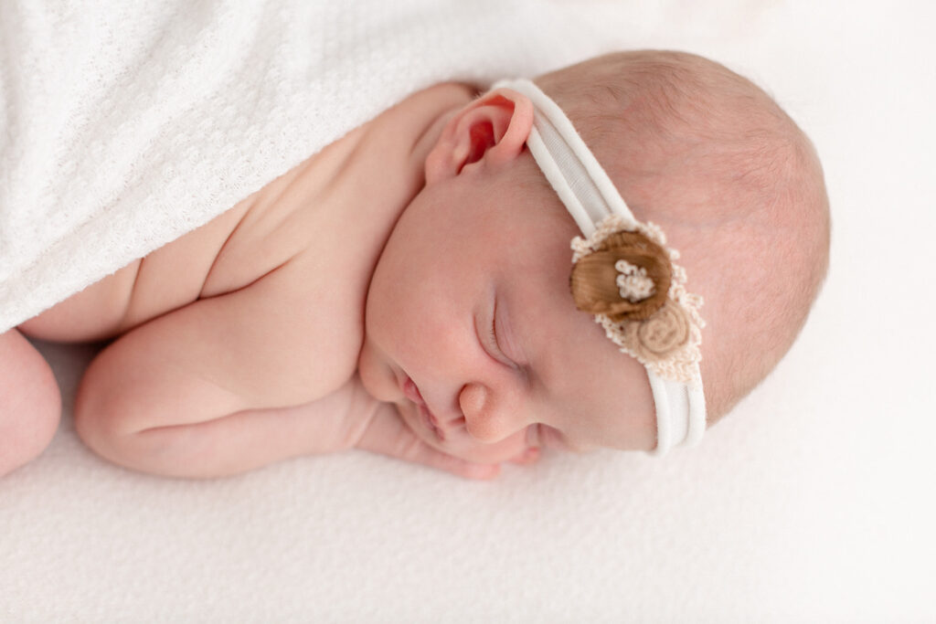 A newborn baby sleeps on a white bed in a fabric headband Posh Baby Portland