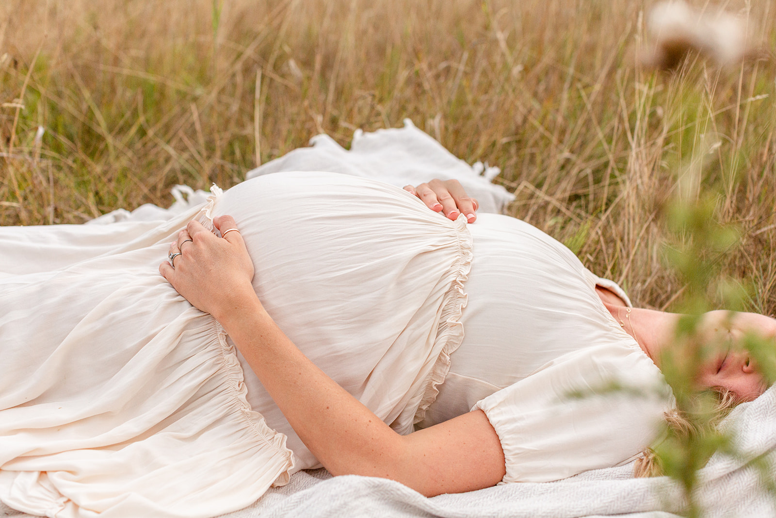 Profile of a mother to be laying in the tall grass while holding her bump in a white dress after getting 3D Ultrasound Portland