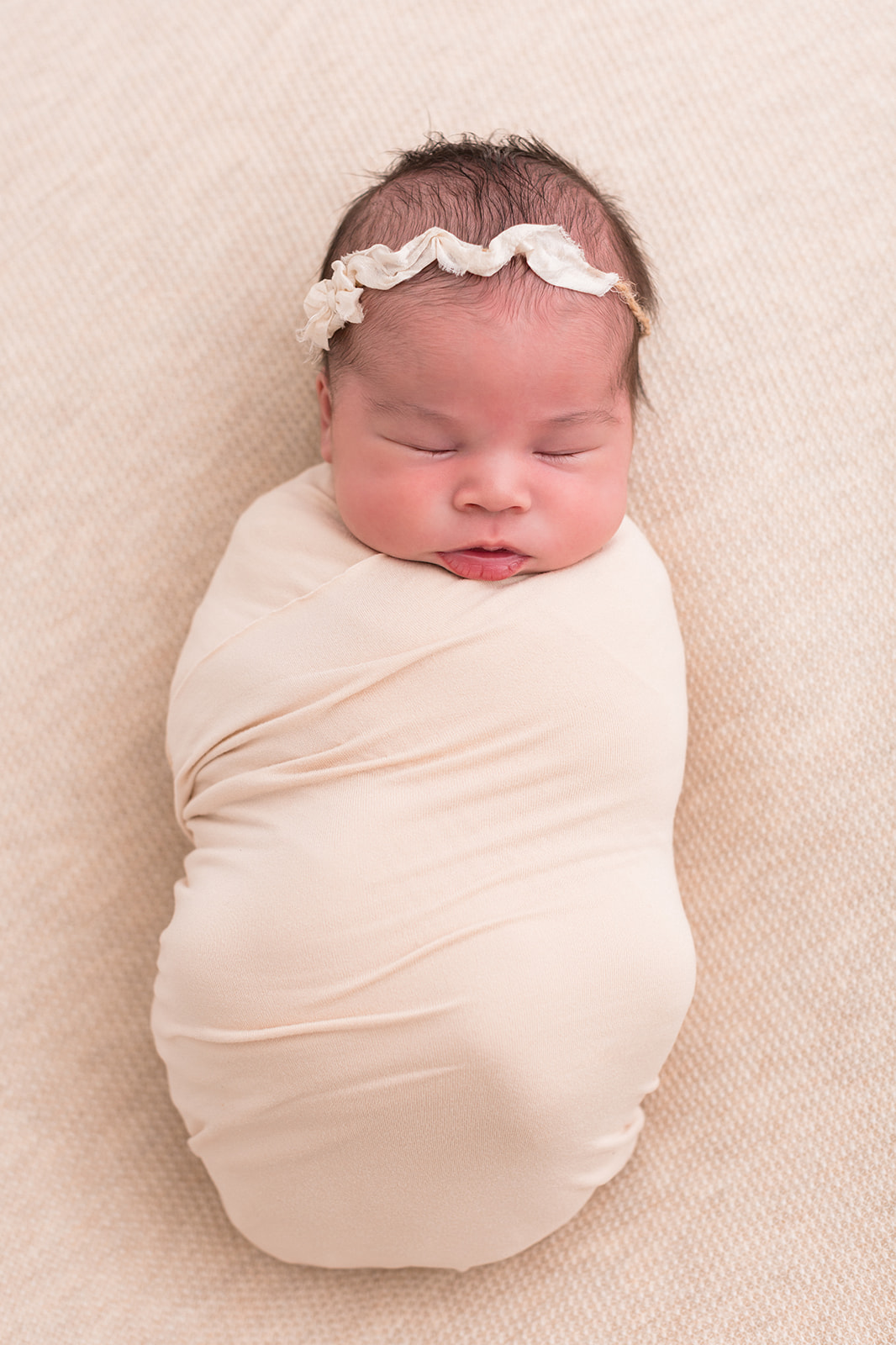 A newborn baby girl sleeps in a beige swaddle in a studio after using Portland OBGYN