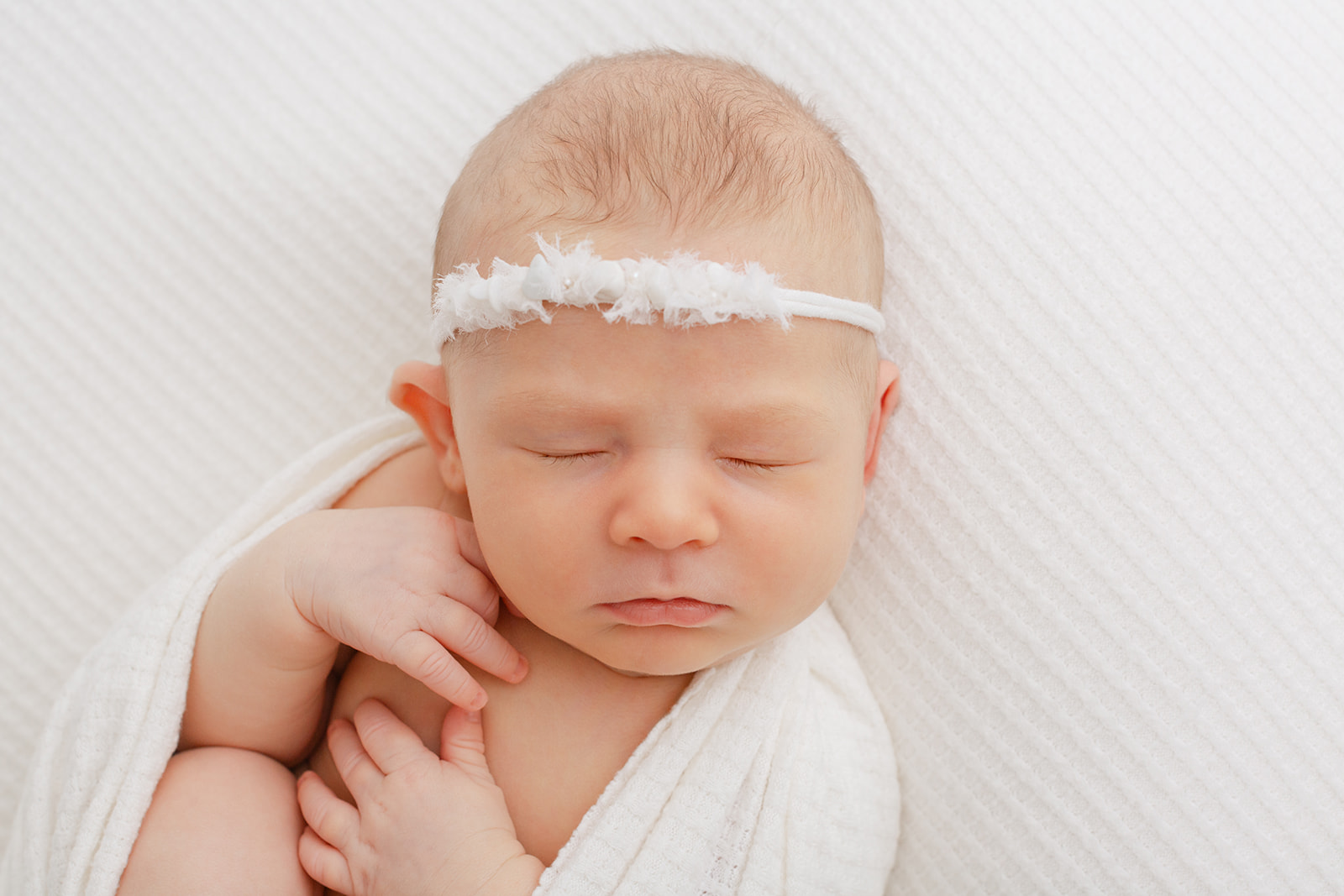 A newborn baby sleeps in a white headband in a studio