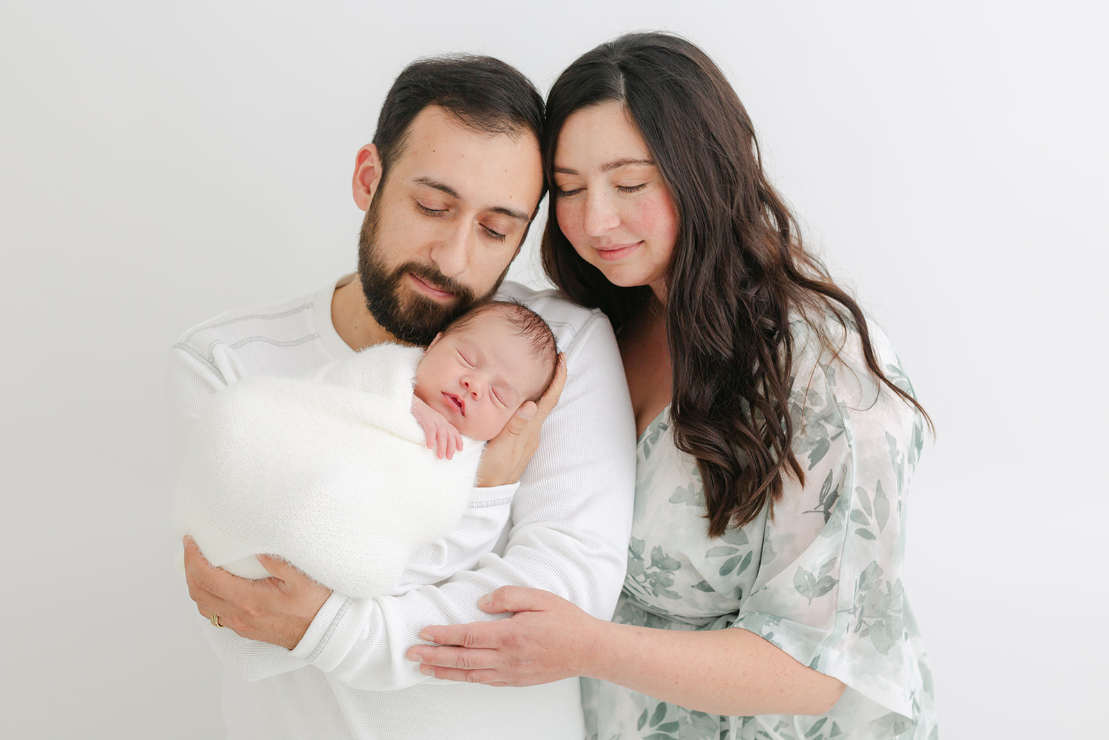 Happy new parents cradle their sleeping newborn baby while standing in a studio