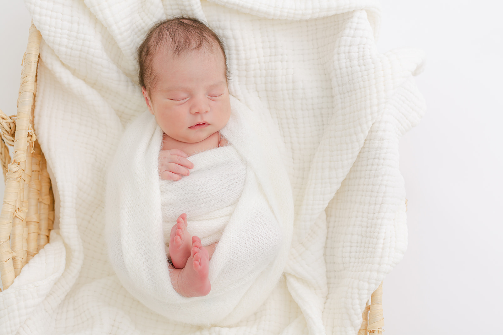 A newborn baby baby sleeps in a knit swaddle and woven basket in a studio thanks to Fertility Acupuncture Portland