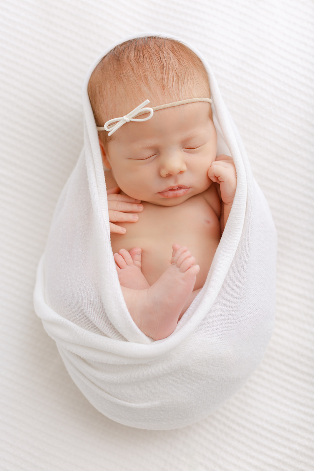 A newborn baby sleeps in an open white swaddle on a bed in a studio after Fertility Acupuncture Portland