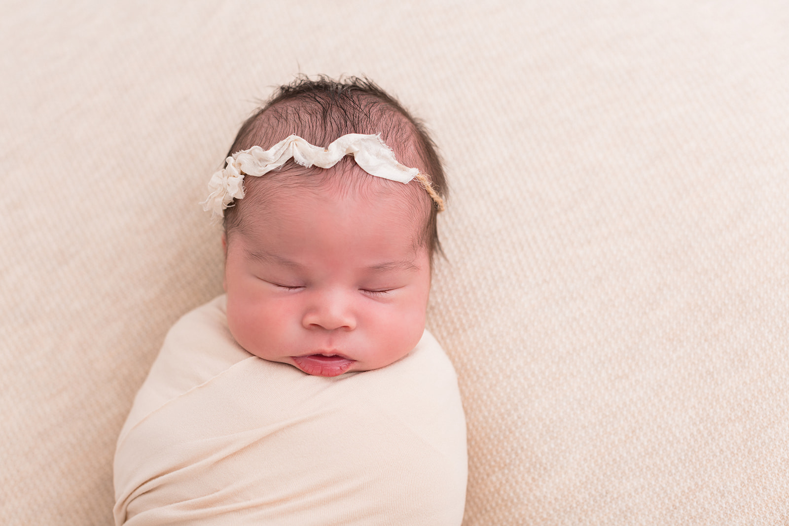 A newborn baby girl in a white fabric headband sleeps in a swaddle in a studio thanks to Portland Parenting classes
