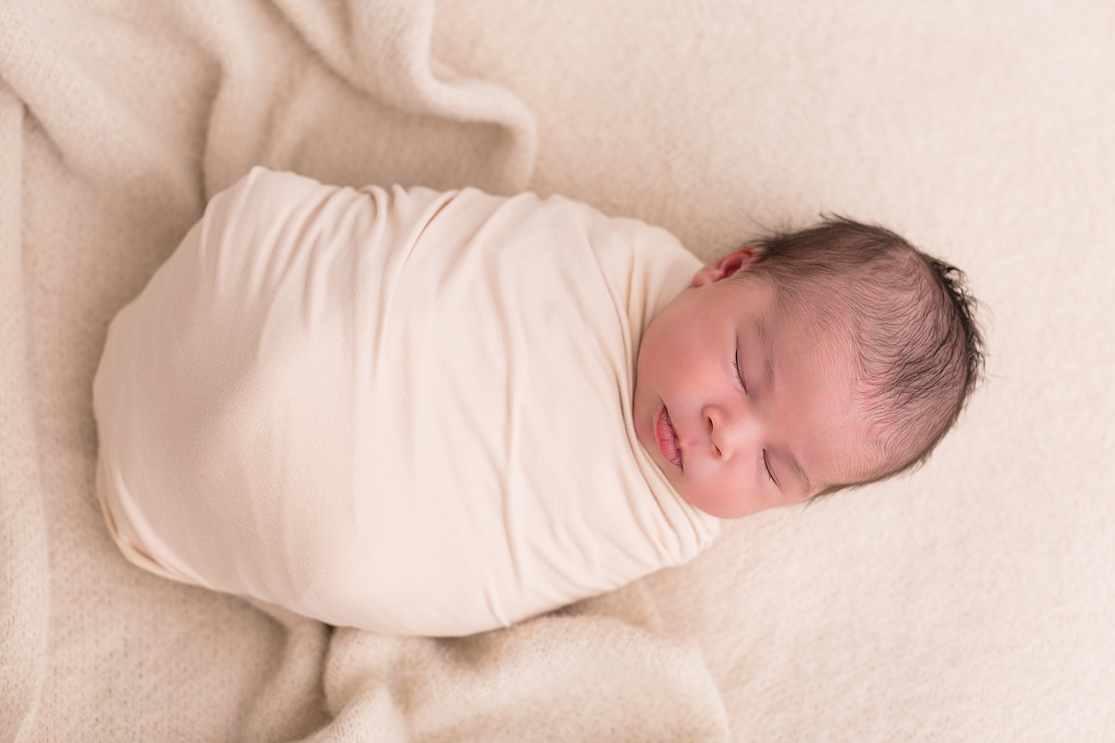 A newborn baby sleeps in a white swaddle in a studio after attending Portland Parenting classes