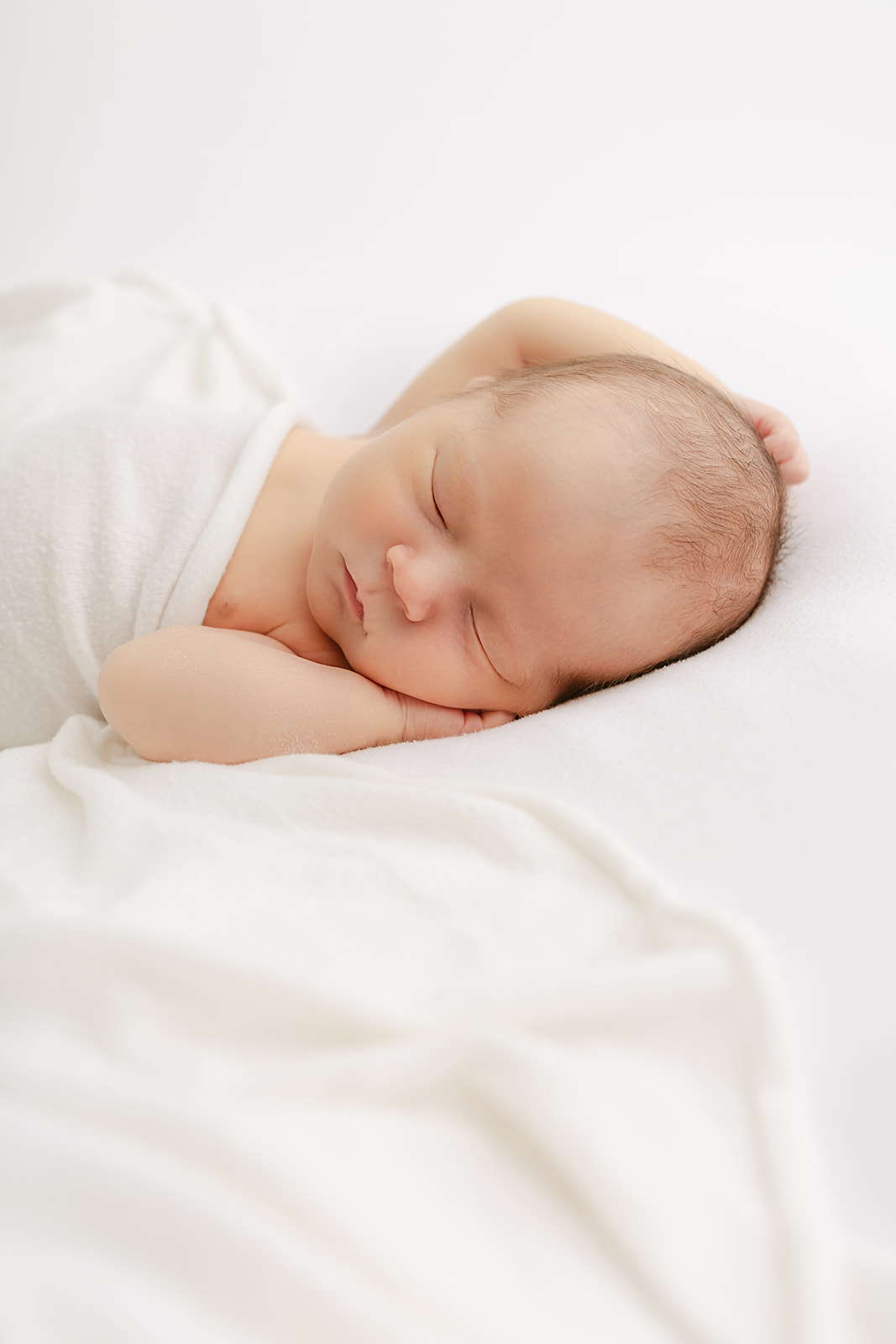 A newborn baby relaxes on a white bed in a studio