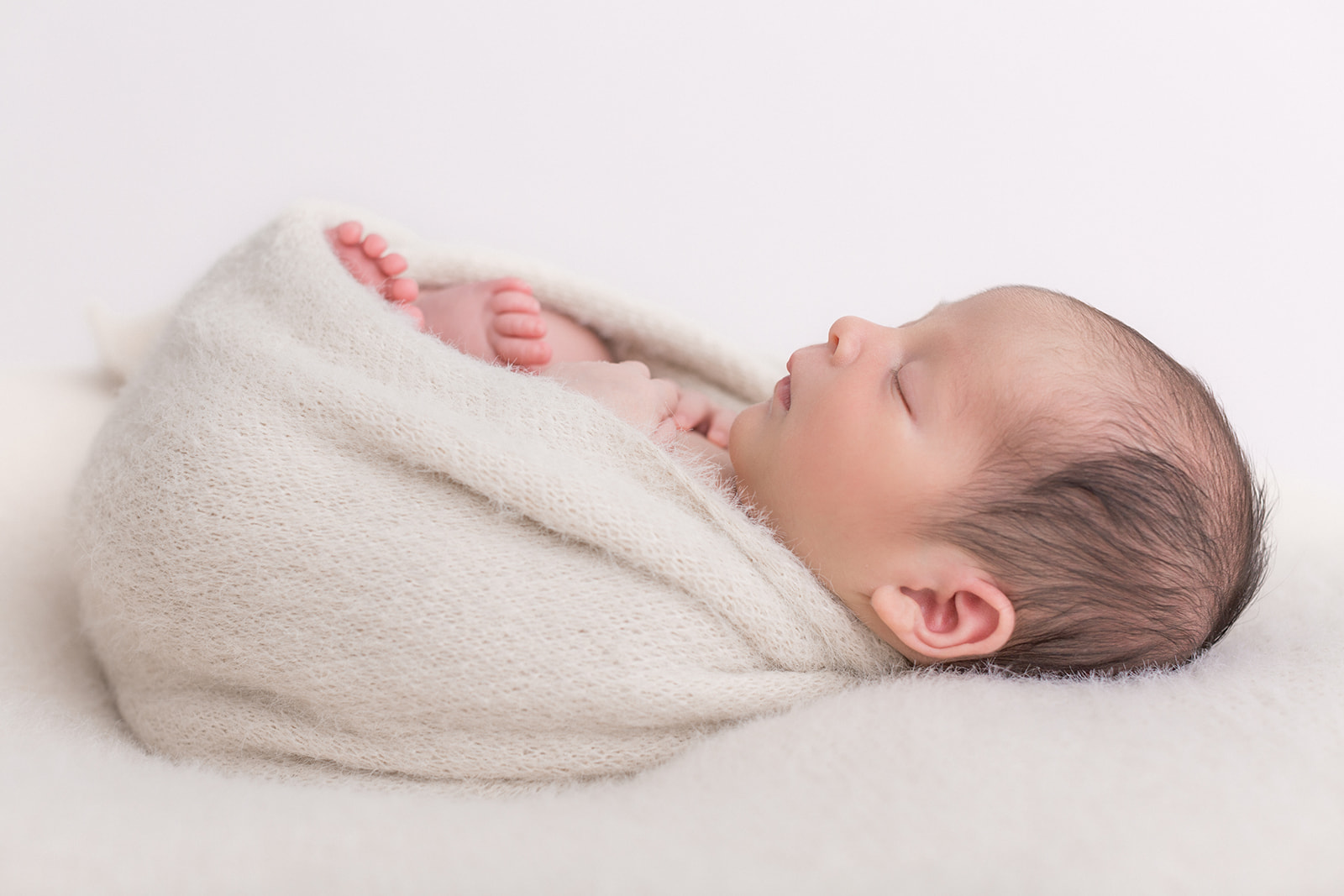 A newborn baby sleeps in a white knit swaddle on a white bed before some baby classes in Portland