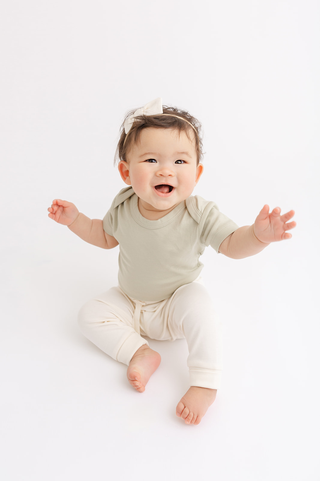 A happy toddler girl smiles while playing on the floor of a studio in a green shirt and white pants