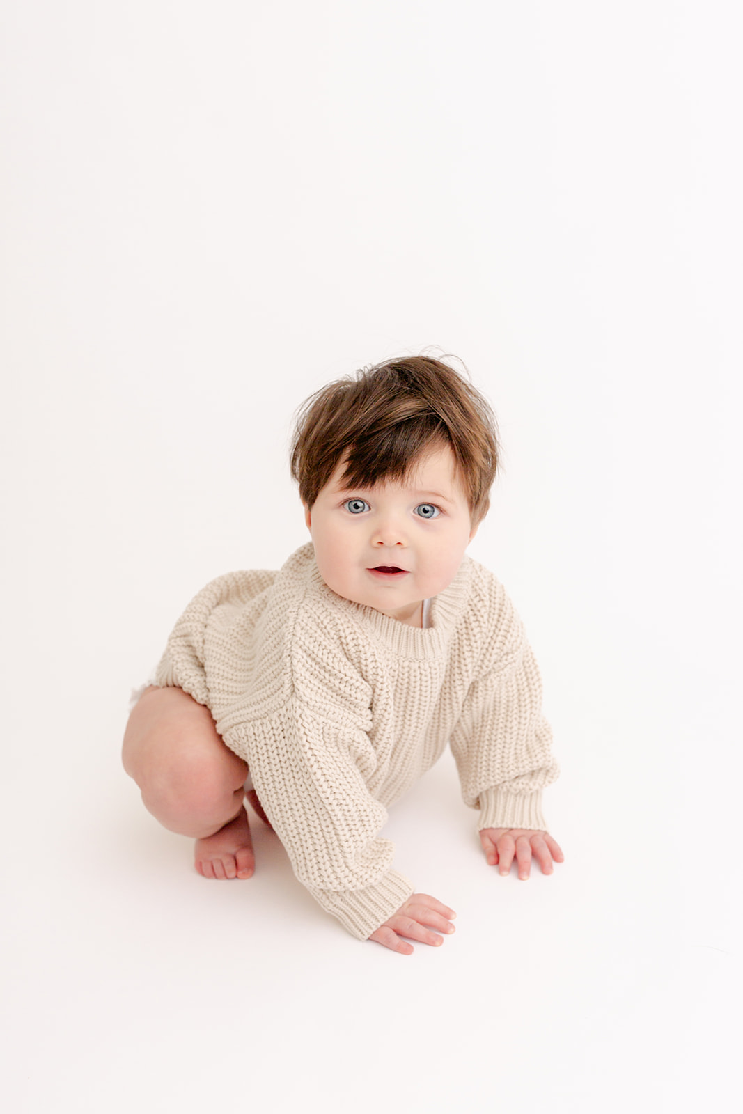 A toddler boy in a knit sweater crawls through a white studio before some Baby yoga Portland