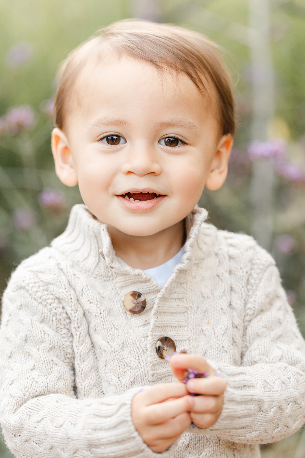 A happy toddler boy explores a garden in a cream knit sweater before visiting an indoor playgrounds in Portland