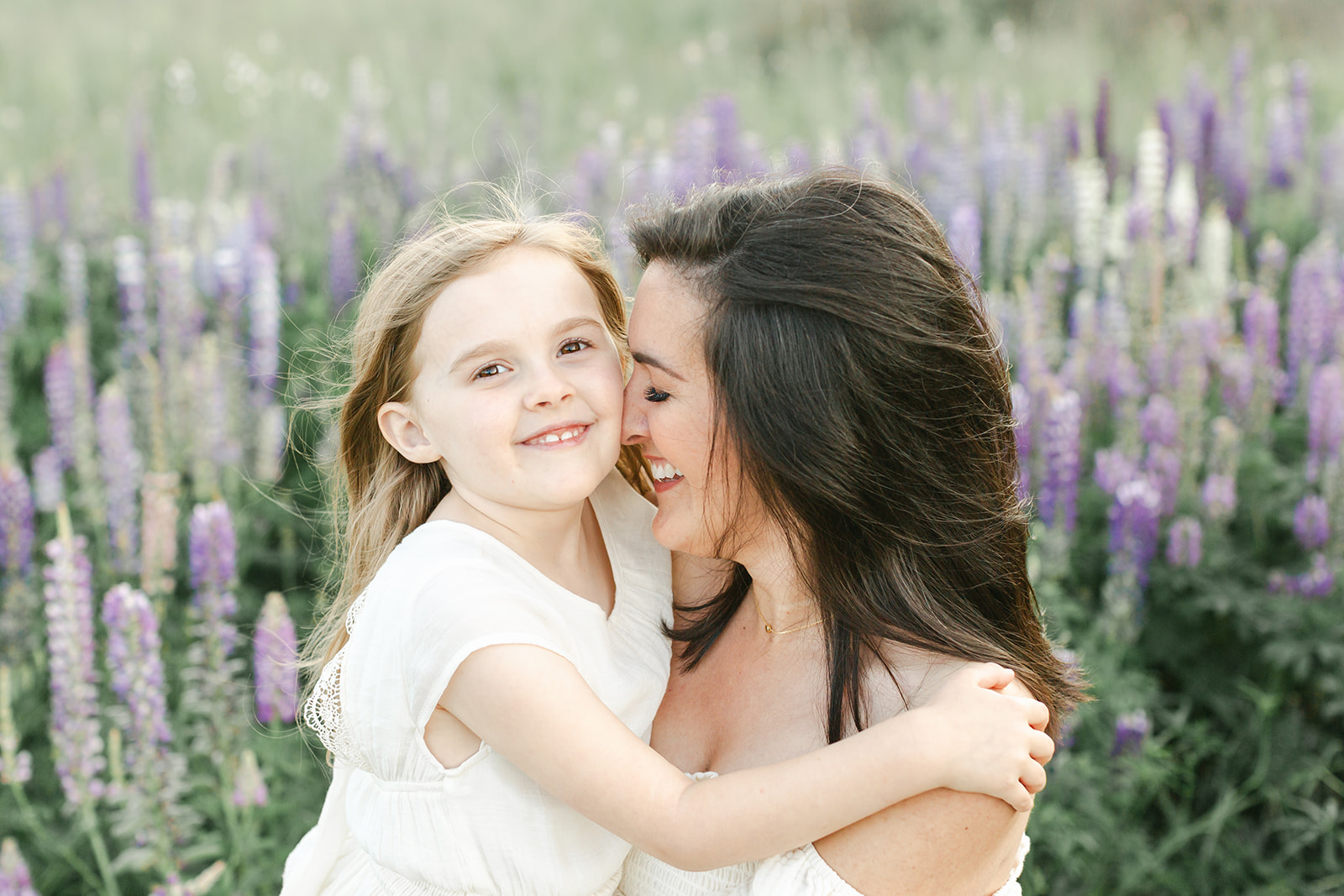 A mother snuggles and laughs with her young daughter in a field of purple wildflowers before visiting Portland Toy Stores