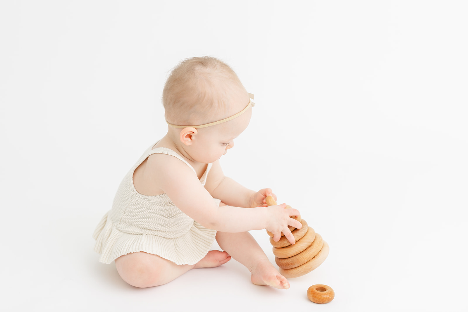 A toddler girl in a dress sits on the floor of a studio playing with a wooden stacker toy after visiting The Wiggle Room Portland