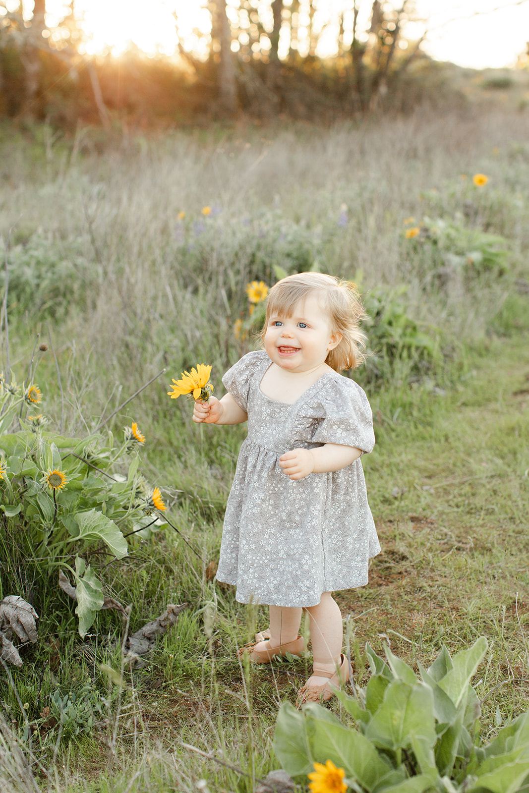 A toddler girl picks flowers while exploring a trail in a dress during toddler activities Portland