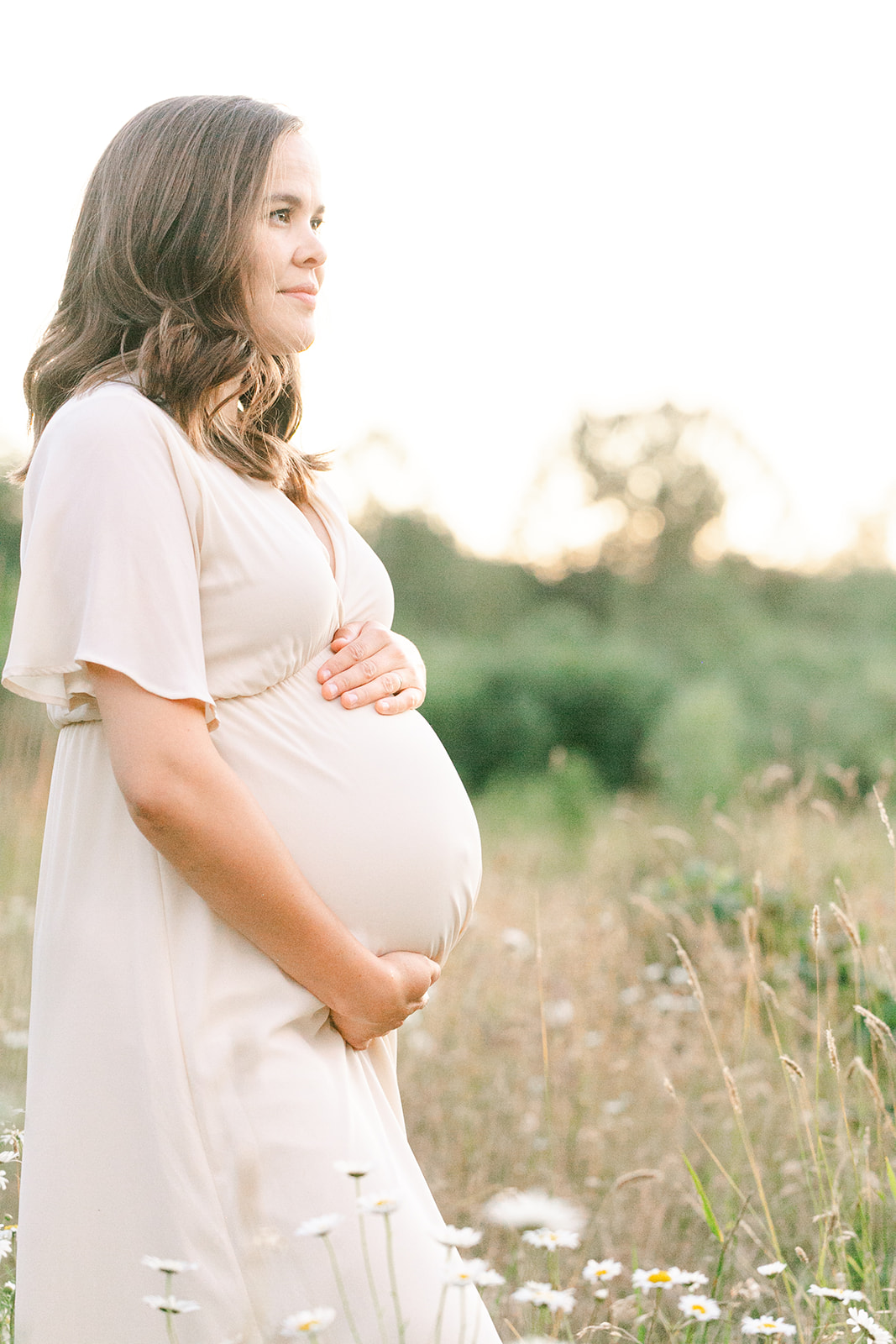 A mom to be explores a field of wildflowers at sunset in a pink maternity gown after visiting Birth First Doulas