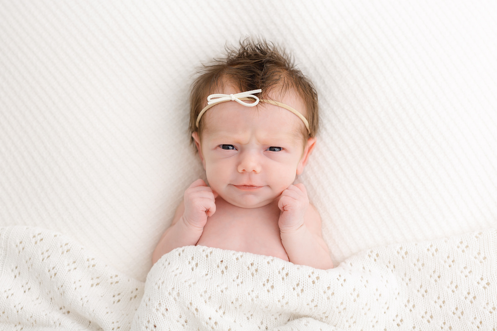 A newborn baby makes a squish face while laying under a white blanket after using Alma Midwifery