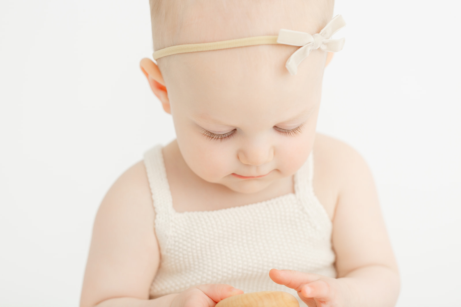 A young baby in a white onesie sits in a studio playing with a wooden toy after using Unfurling Birth