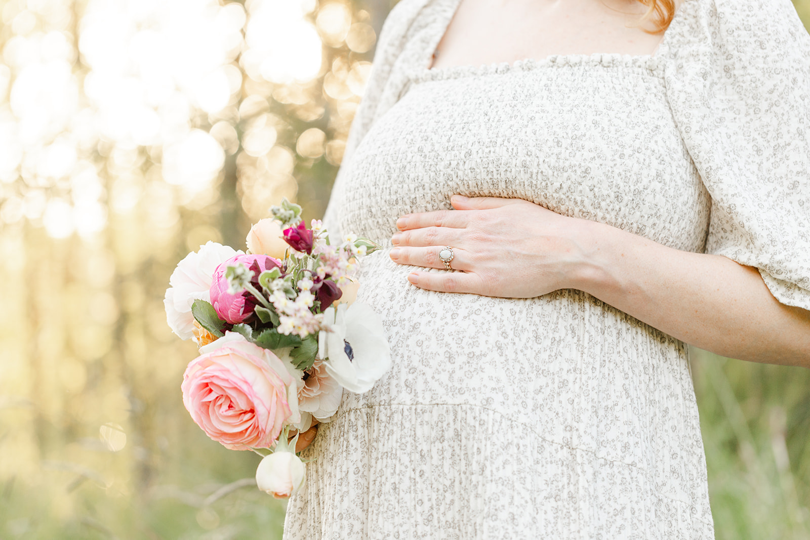 Details of a mom to be holding a bouquet and her bump in a forest at sunset