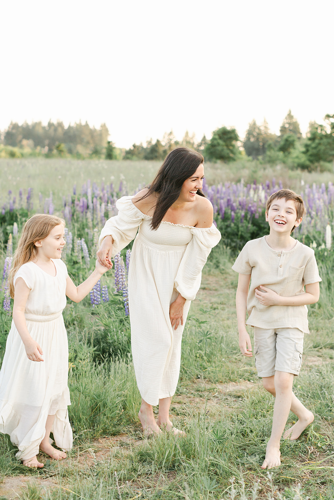 A happy mom laughs with her young daughter and son in a field of wildflowers