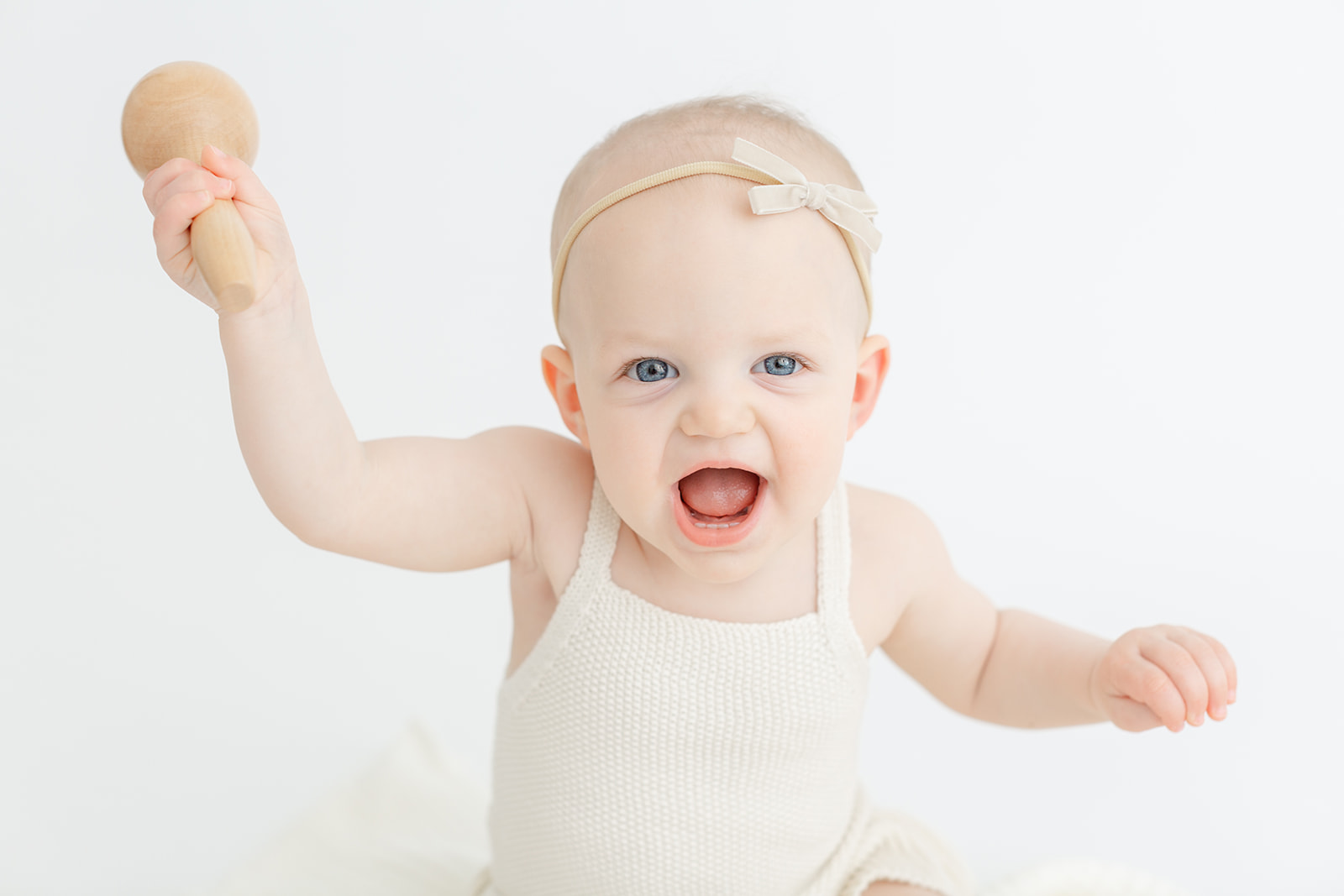 A toddler girl plays with a wooden maraca toy while sitting in a studio after meeting PDX Doulas