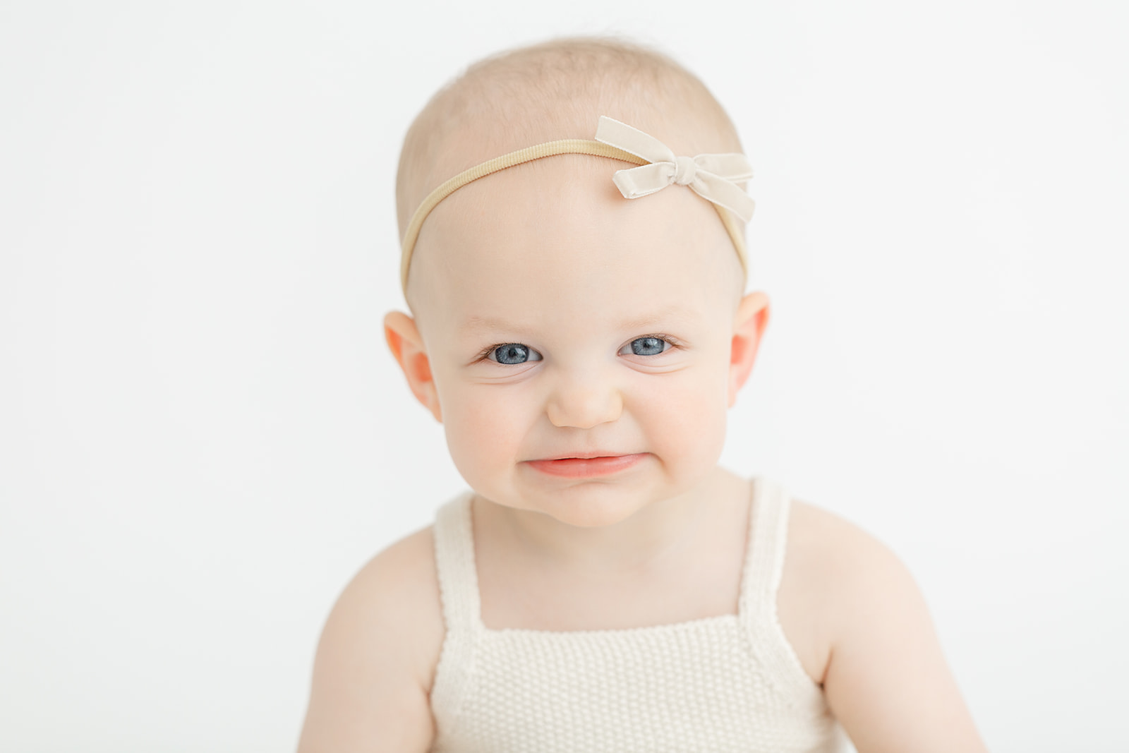 A toddler girl in a white dress makes a silly face while sitting in a studio after meeting PDX Doulas