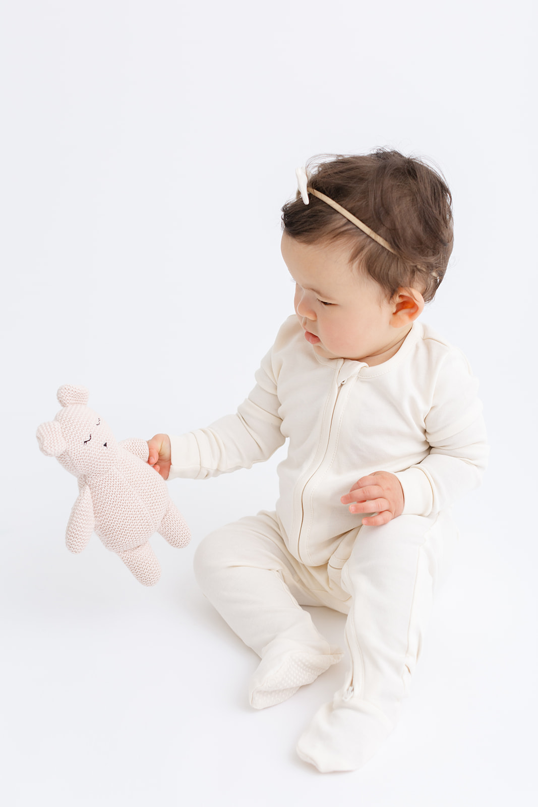 A toddler in a white onesie plays with a stuffed animal on the floor of a studio before visiting Ready Set Grow