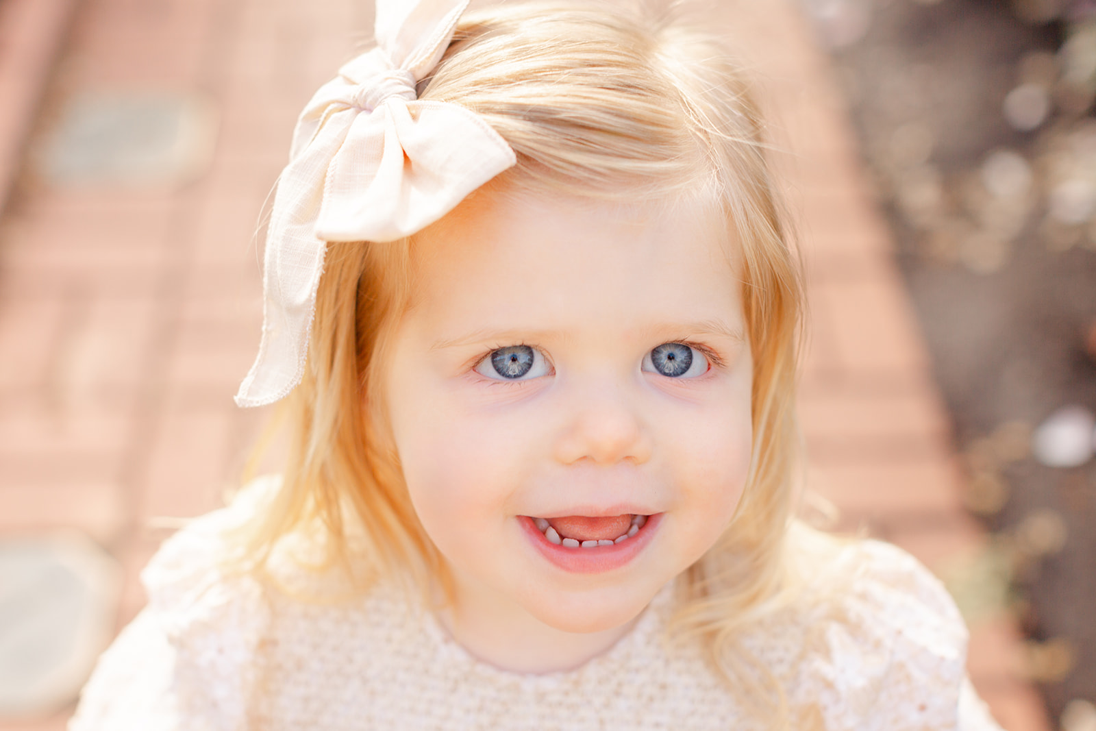 Close up of a toddler girl in a dress on a brick garden path at sunset