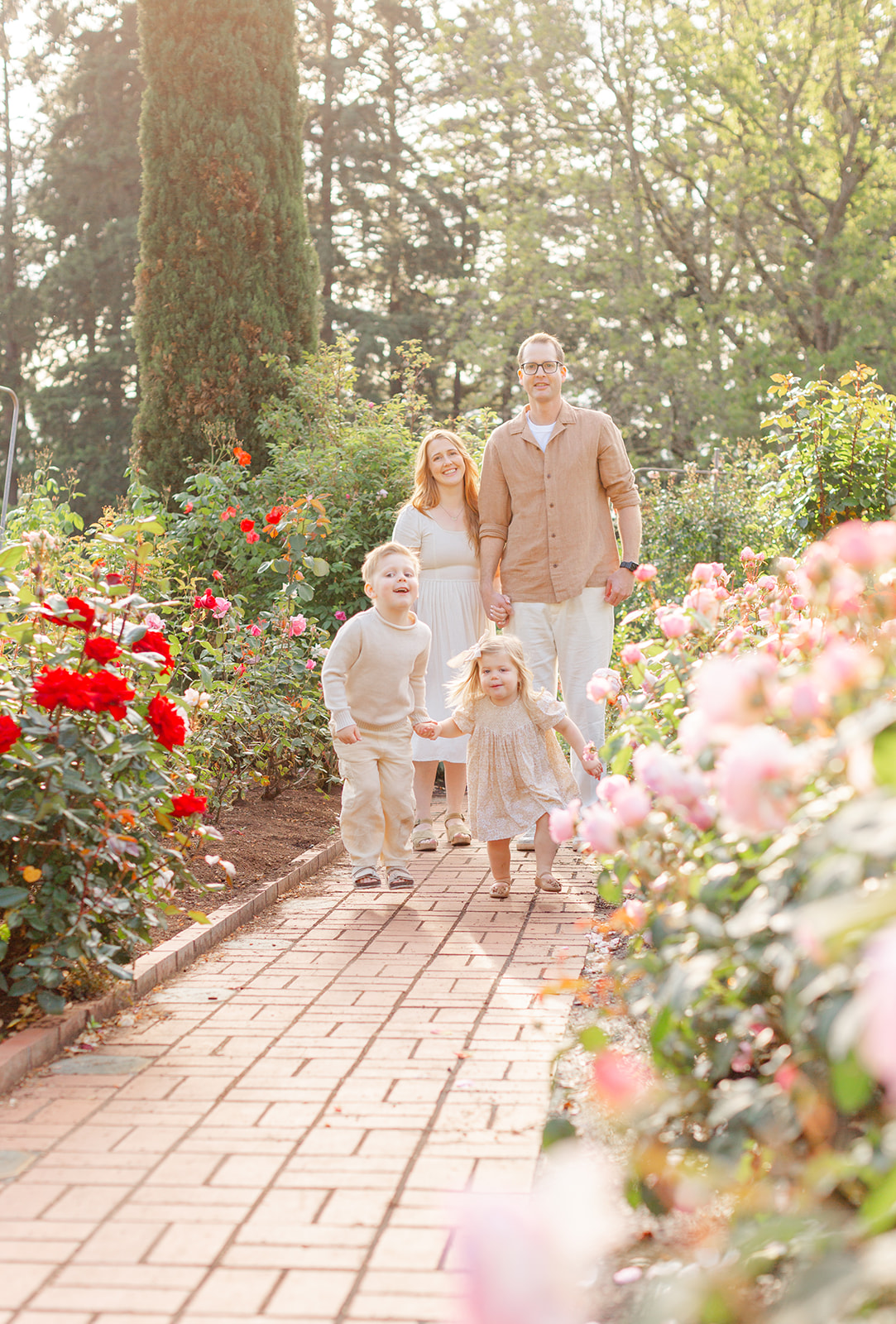 A happy family of 4 hold hands while exploring a colorful rose garden after meeting A Brilliant Nanny