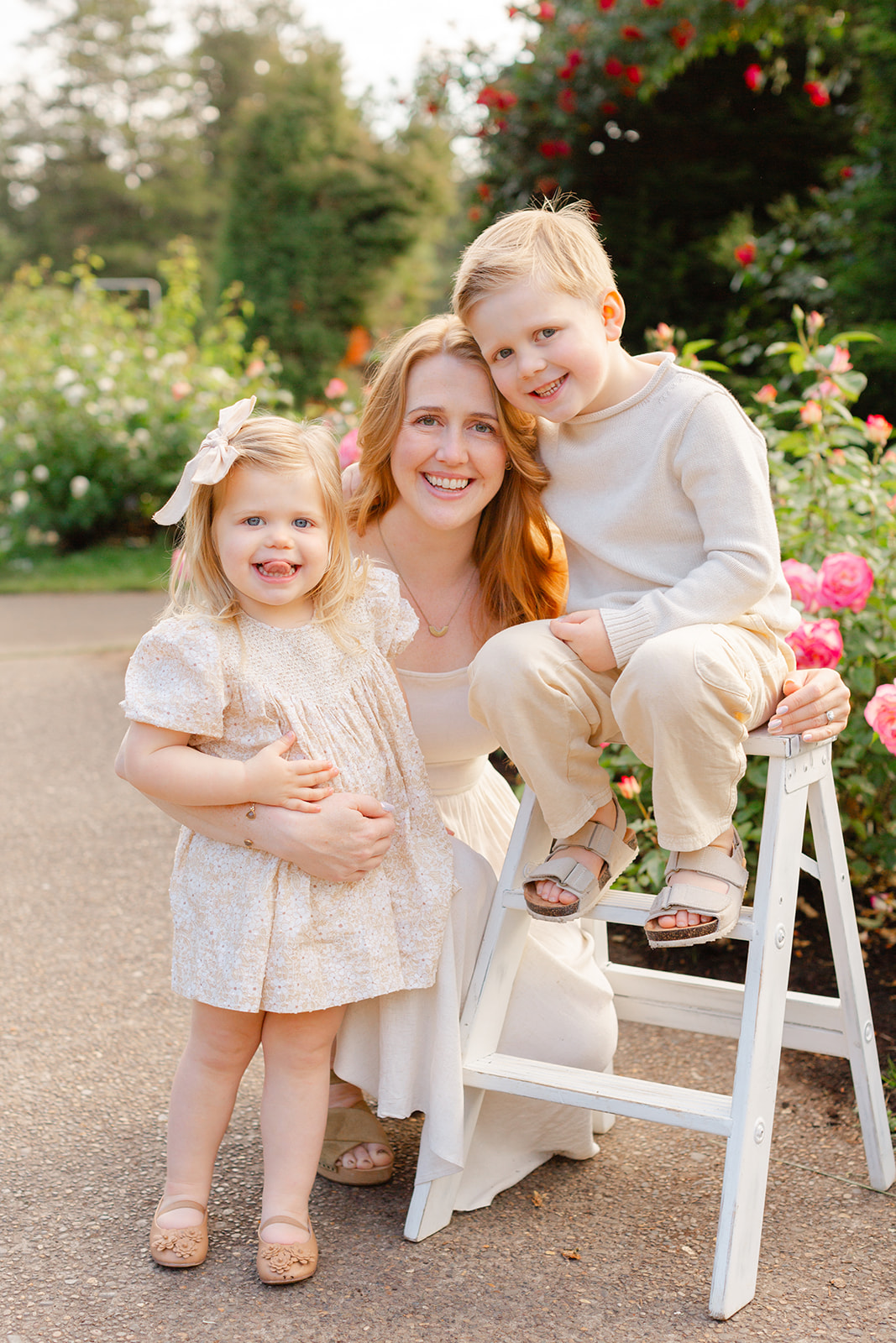 Happy toddler brother and sister hug mom and smile while exploring a rose garden after meeting A Brilliant Nanny